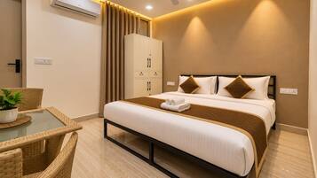 Una habitación de hotel con una cama, un armario, una mesa con una planta y un ventilador de techo.