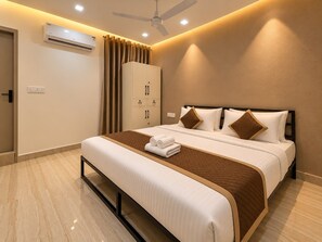 A hotel room with a bed, a wardrobe, an air conditioning unit, a ceiling fan, and a bathroom door.