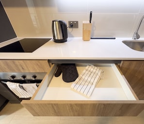 A kitchen with a stainless steel kettle, a knife block, and a drawer with oven mitts and a striped cloth. - Edificio Quinta Vista by Domus Travels (Quinta Normal)