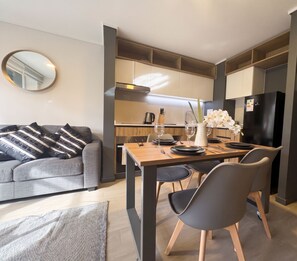 A modern kitchen with a dining area, a grey sofa, and a mirror on the wall. - Edificio Quinta Vista by Domus Travels (Quinta Normal)