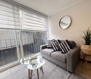 A modern living room with a grey sofa, a glass coffee table, and a round mirror on the wall. - Edificio Quinta Vista by Domus Travels (Quinta Normal)