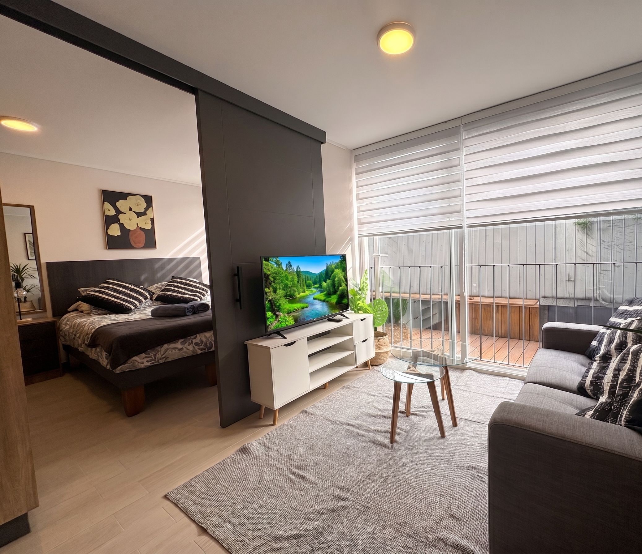 A modern living room with a bed, sofa, TV, and a balcony with a view.