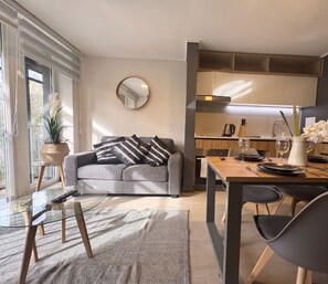 A modern living room with a grey sofa, a round mirror, and a dining area with a wooden table set for two. - Edificio Quinta Vista by Domus Travels (Quinta Normal)