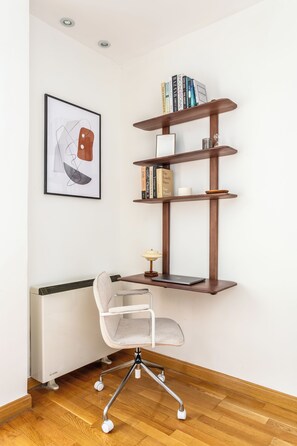 A modern office space with a white chair, a wooden desk, and a bookshelf with books and decorative items. - A two-bedroom in Chamberí where full-length windows open onto a balcony view and a large round table seats friends for a long meal, on a street where families have lived for generations. (MADRID)