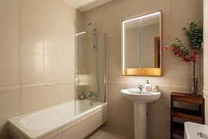 A bathroom with a bathtub, a sink, and a mirror. - A two-bedroom in Chamberí where full-length windows open onto a balcony view and a large round table seats friends for a long meal, on a street where families have lived for generations. (MADRID)