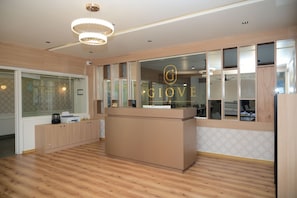 A modern reception area with a wooden reception desk, glass partitions, and a chandelier. - Hotel Giove (Bangalore)