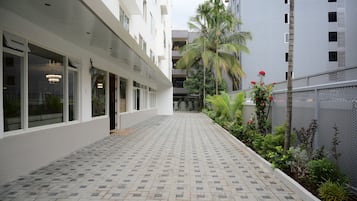 A modern building with a tiled walkway and a small garden area with palm trees and red flowers.