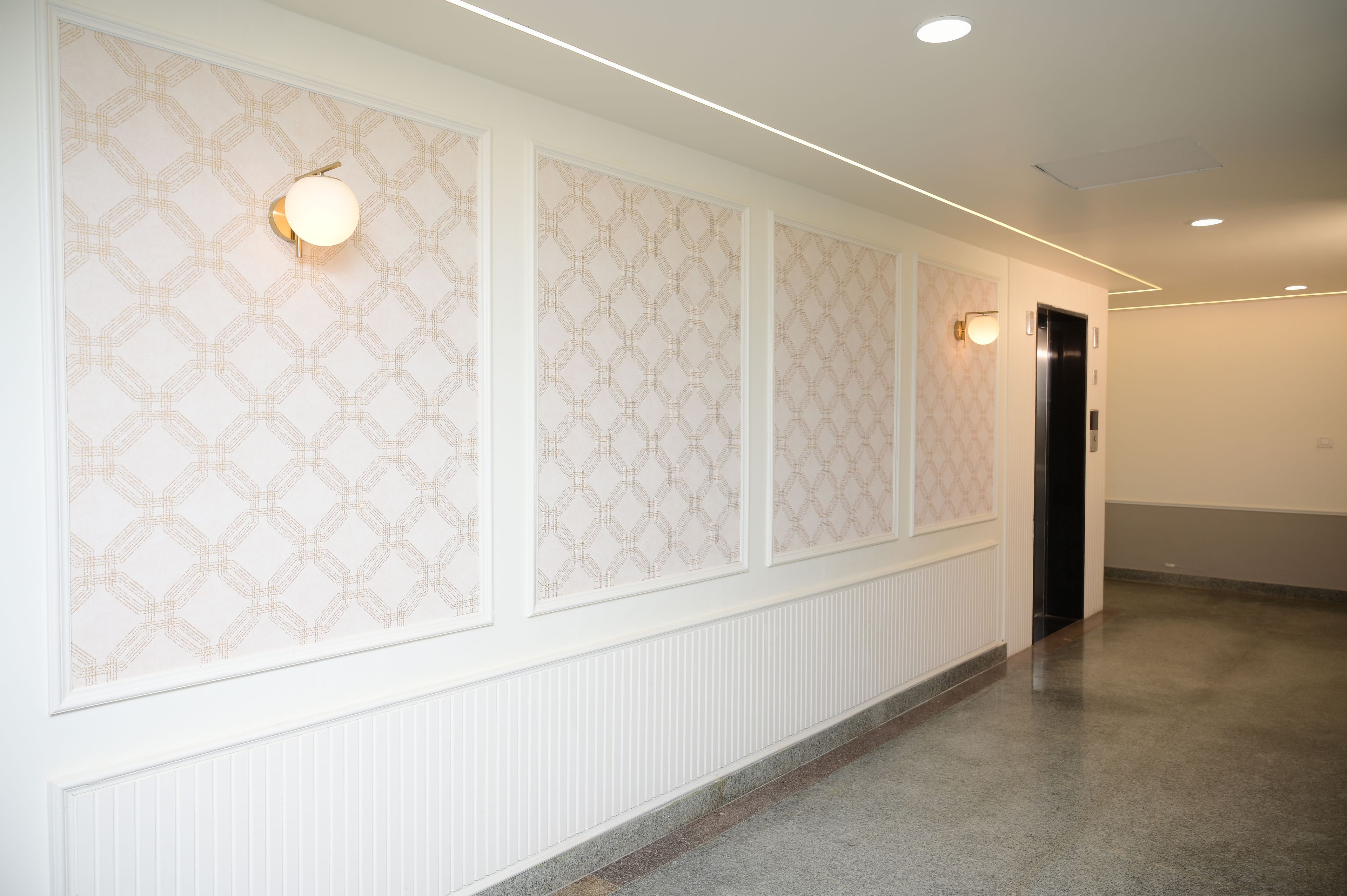 A hallway with patterned wallpaper, recessed lighting, and a door at the end.