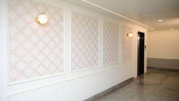 A hallway with patterned wallpaper, recessed lighting, and a door at the end.
