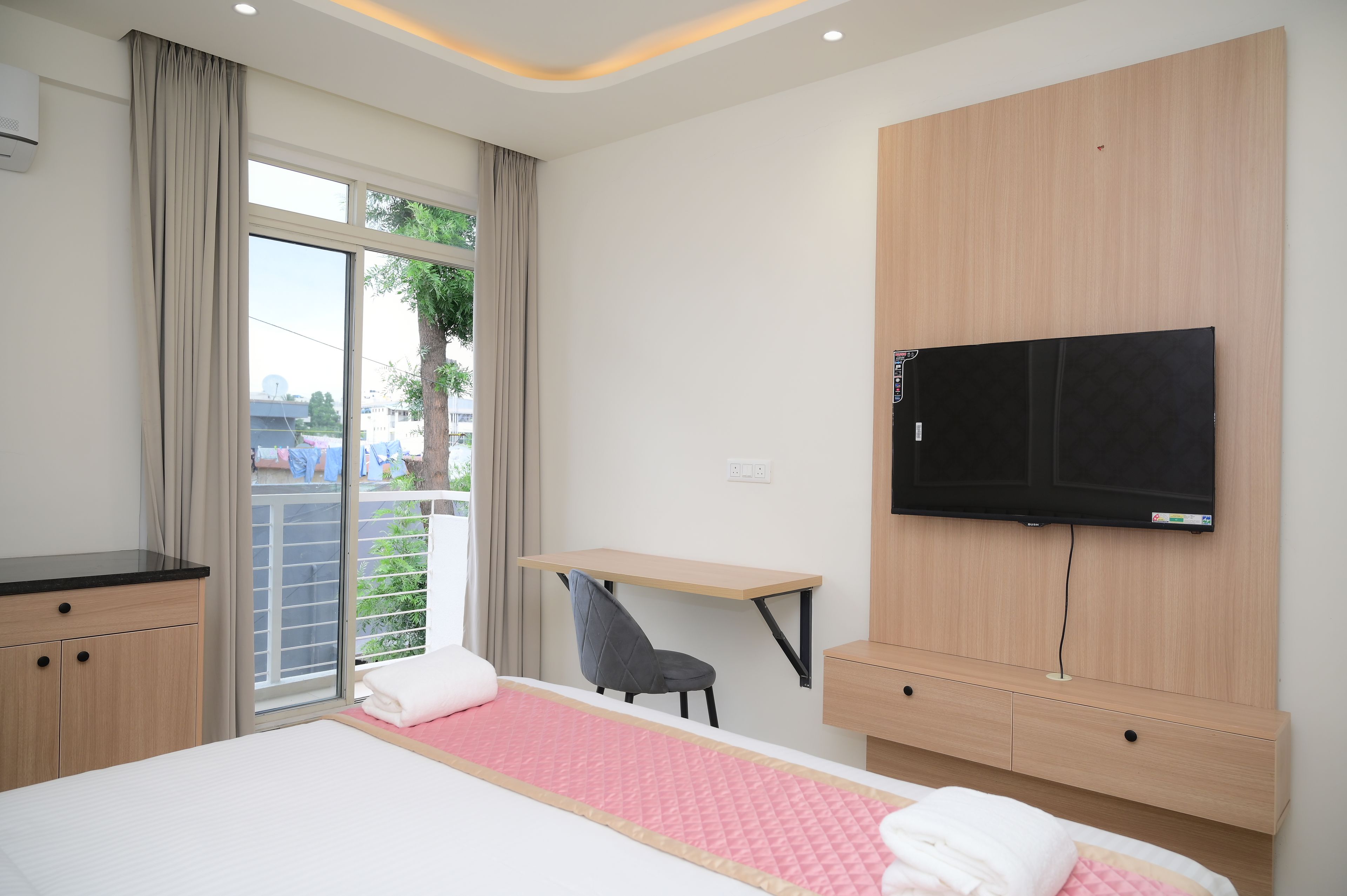 Una camera d'albergo con un letto, una scrivania, una sedia, una televisione e una finestra con tende.