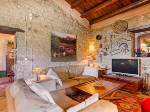 A cozy living room with a stone wall, a large painting, a television, and a wooden coffee table. - Country house 'Casa Vinzeria' with private pool, private terrace and Wi-Fi (Castelbuono)