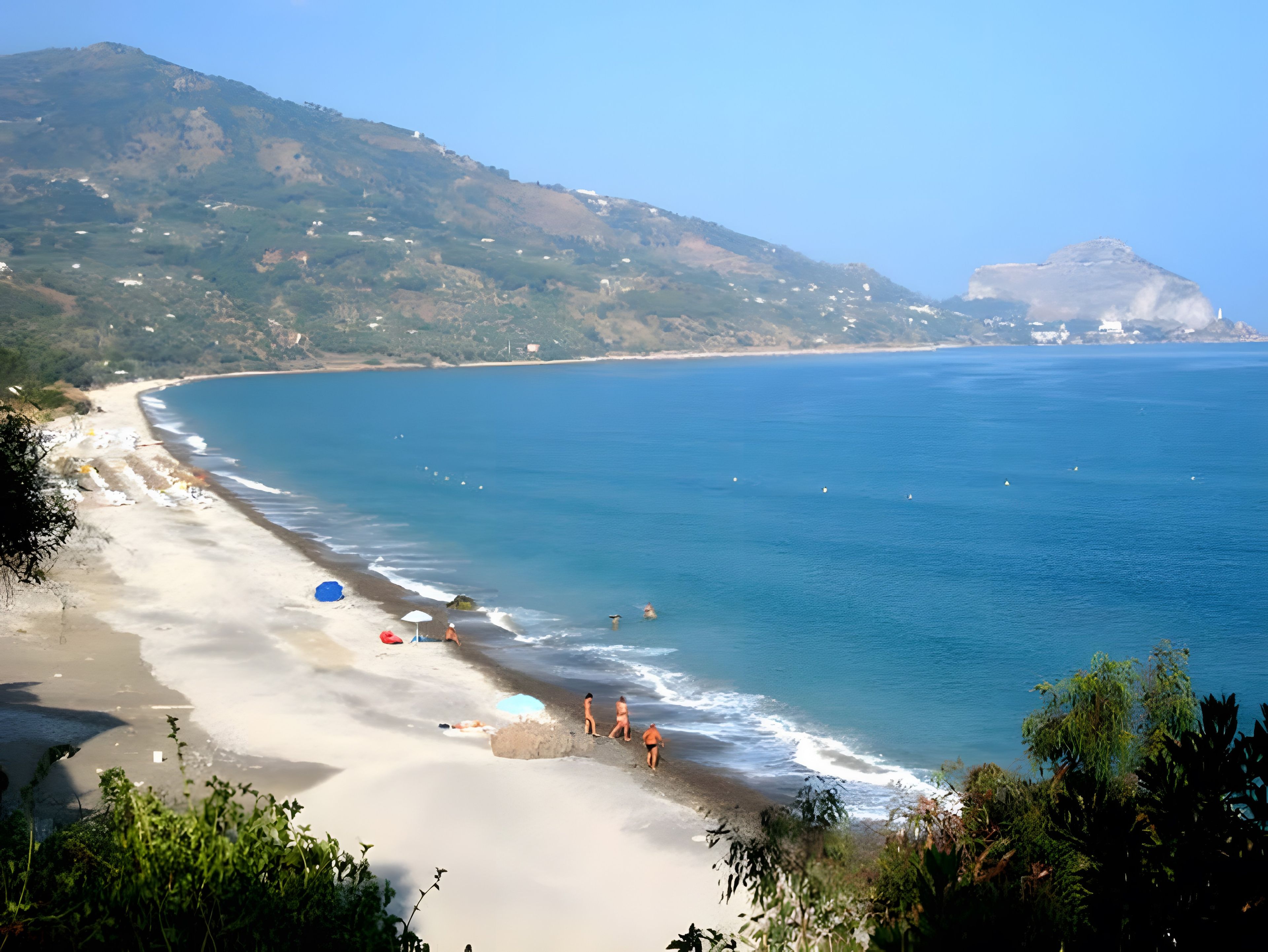 Una playa con aguas cristalinas, una orilla arenosa y un telón de fondo montañoso.