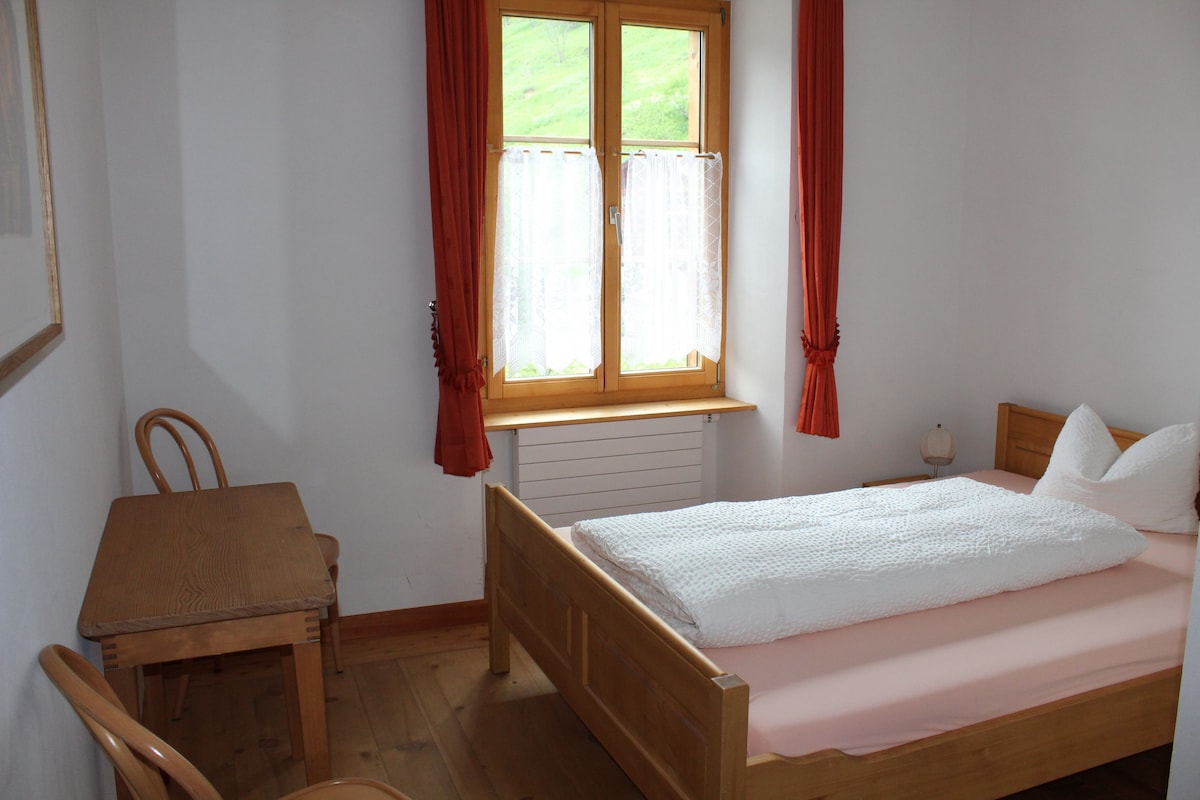 A bedroom with a wooden bed, a wooden desk, and a window with curtains.