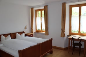 A bedroom with a wooden bed, a desk, and a chair. There are two windows with curtains. - Hotel Ofenhorn (Binn)