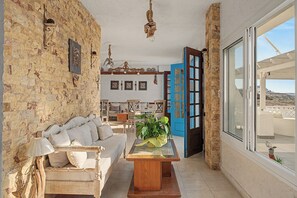 A cozy living room with a stone wall, a wooden sofa, a coffee table, and a view through a blue door. - Apartment 'Pool Suite 1' with Shared Pool and Balcony (Αρκάσα)
