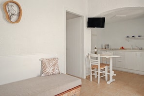 A compact living space with a sofa, a dining table, and a kitchen area. - Apartment 'Pool Suite 1' with Shared Pool and Balcony (Αρκάσα)