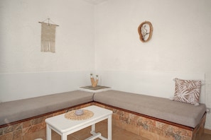 Eine Sitzecke mit Ecksofa, einer Steinwand, einem kleinen Tisch mit gewebter Tischmatte und einer Wanddeko aus Makramee.
