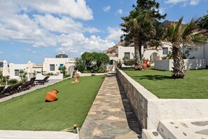 A courtyard with a stone pathway, outdoor seating, and a view of white buildings with blue doors. - Apartment 'Bangalow 1' with Sea View, Wi-Fi and Air Conditioning (Αρκάσα)