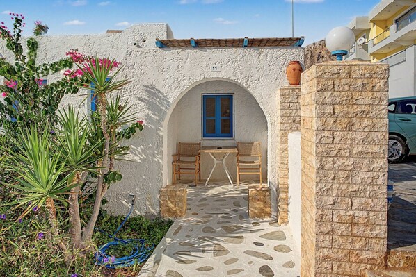 Un patio con suelo de piedra, una mesa de madera con sillas, un ventanal con marco azul y una pared blanca con el número 11.