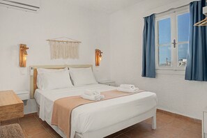A neatly arranged bedroom with a bed, bedside tables, a bedside lamp, and a window with curtains. - Apartment 'Bangalow 1' with Sea View, Wi-Fi and Air Conditioning (Αρκάσα)