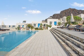 Zona de piscina con sillones de descanso y montañas al fondo.