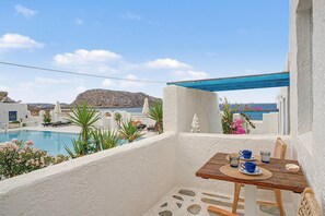 Een balkon met uitzicht op een zwembad, een tafel met blauwe bekers en een glas, en een blauwe pergola.