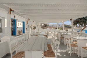An outdoor seating area with white tables and chairs, a covered roof, and a view of buildings in the distance. - Apartment 'Pool Suite 5' with Sea View, Wi-Fi and Air Conditioning (Αρκάσα)