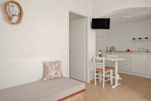 A small, cozy room with a sofa, a dining table with chairs, a kitchen area with a TV, and a door leading to another room. - Apartment 'Pool Suite 5' with Sea View, Wi-Fi and Air Conditioning (Αρκάσα)