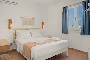 Une chambre à coucher bien rangée, avec un lit, des tables de chevet, une lampe de chevet et une fenêtre avec des rideaux.