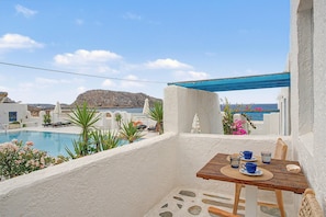Un balcon donnant sur une piscine, une table avec des tasses et un verre bleus, et une pergola bleue.