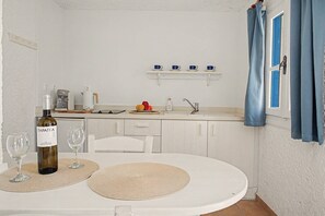 A kitchen with white cabinets, a dining table with placemats, a wine bottle, and glasses. - Apartment 'Pool Suite 8' with Shared Pool and Balcony (Αρκάσα)