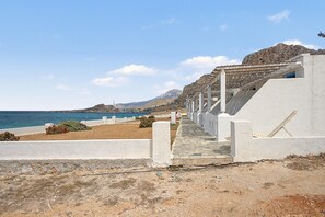 A coastal pathway leading to a white building with a tiled roof, overlooking the sea and a mountainous backdrop. - Studio 'Thalassa Suite 1' with Sea View and Shared Pool (Αρκάσα)