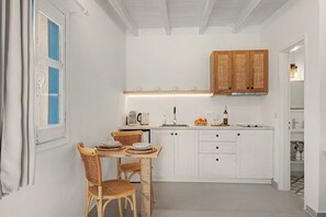 A compact kitchen with white cabinetry, a dining table with chairs, and a small countertop with a coffee maker and fruit. - Studio 'Thalassa Suite 1' with Sea View and Shared Pool (Αρκάσα)