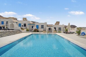 A swimming pool with a clear blue water surface, surrounded by a white building with blue doors and windows, and a stone staircase leading to the pool area. - Studio 'Thalassa Suite 1' with Sea View and Shared Pool (Αρκάσα)
