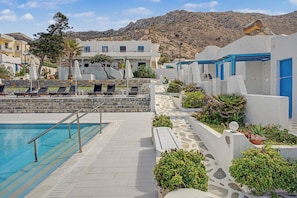 A pool area with lounge chairs, a stone wall, and a mountain backdrop. - Studio 'Thalassa Suite 1' with Sea View and Shared Pool (Αρκάσα)