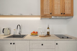 A modern kitchen with a sink, a kettle, a bottle of dish soap, a plate of fruit, wine glasses, and a wine bottle. - Studio 'Thalassa Suite 1' with Sea View and Shared Pool (Αρκάσα)