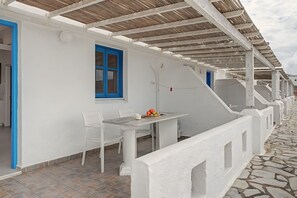 Ein weißes Gebäude mit überdachter Außenbestuhlung, einer blauen Tür und einem Fenster mit Vorhang.