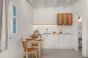 A compact kitchen with white cabinetry, a dining table with chairs, and a small countertop with a kettle and coffee maker. - Studio Apartment 'Thalassa Suite 3' with Sea View and Shared Pool (Αρκάσα)
