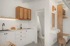 A modern kitchen with white cabinetry, a wooden cabinet with a woven door, a built-in sink, and a countertop with fruit and a wine bottle. - Studio Apartment 'Thalassa Suite 3' with Sea View and Shared Pool (Αρκάσα)