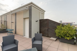 Une terrasse sur le toit, aménagée avec du mobilier d’extérieur, quelques plantes en pot et offrant une vue sur le panorama urbain.