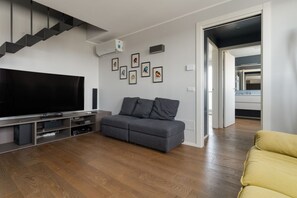 Un salon moderne avec un téléviseur à écran plat, un canapé gris, un plancher en bois et un escalier.
