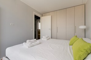A bedroom with a bed, pillows, a wardrobe, and a door leading to another room. - A modern and bright 50 sqm one-bedroom apartment with a terrace, suitable for two guests and located near the San Siro Stadium. Situated on the eighth floor of a building (with elevator —though NOT suitable for people with disabilities due to a few ste (Milan)