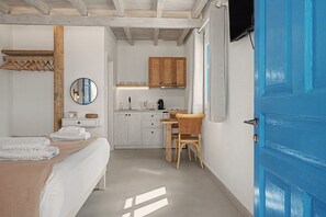 A bedroom with a bed, a bedside table, a mirror, and a wardrobe. There is a kitchenette with a stove, a chair, and a table. - Studio Apartment 'Thalassa Suite 6' with Sea View and Shared Pool (Αρκάσα)