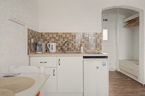 Eine kleine Küche mit Fliesenrückwand, einer Kaffeemaschine, einem Wasserkocher und einem Geschirrspüler.