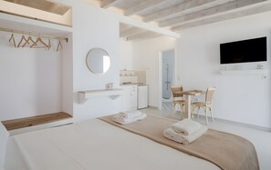 Ein modernes Hotelzimmer mit Bett, kleinem Schreibtisch, Stuhl, Fernseher und einem Badezimmer mit Dusche.