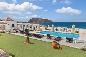 Ein Poolbereich mit Liegestühlen und Sonnenschirmen, mit freiem Blick auf das Meer und einer bergigen Kulisse.