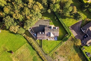 Eine Vogelperspektive eines großen, mehrstöckigen Hauses mit einem weitläufigen Garten, umgeben von üppiger Vegetation.