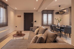 A modern living room with a sectional sofa, a dining area with a table and chairs, and a kitchen in the background. - Villa Verde Zante - Three Bedroom Villa, Sleeps 7 (Kallithea)