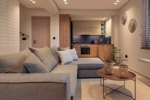 A modern living room with a sectional sofa, a small round table, and a kitchen in the background. - Villa Verde Zante - Three Bedroom Villa, Sleeps 7 (Kallithea)