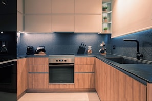 A modern kitchen with wooden cabinets, a black countertop, and a blue backsplash. - Villa Verde Zante - Three Bedroom Villa, Sleeps 7 (Kallithea)